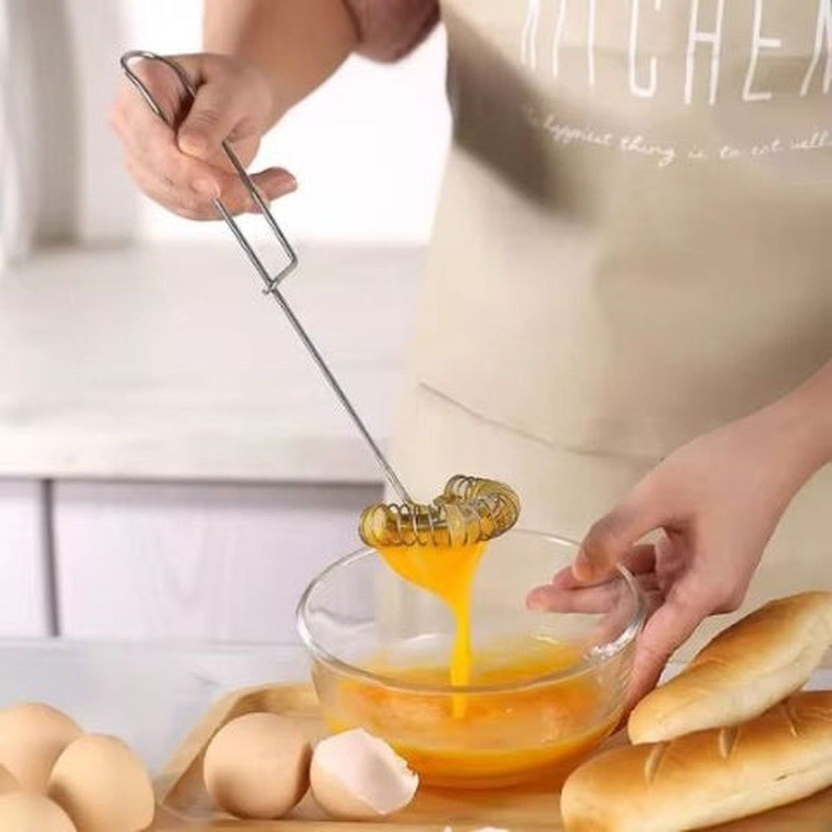 Fouet Savourel en inox tenu par sa boucle, filet d'œuf battu coulant de la spirale dans un bol