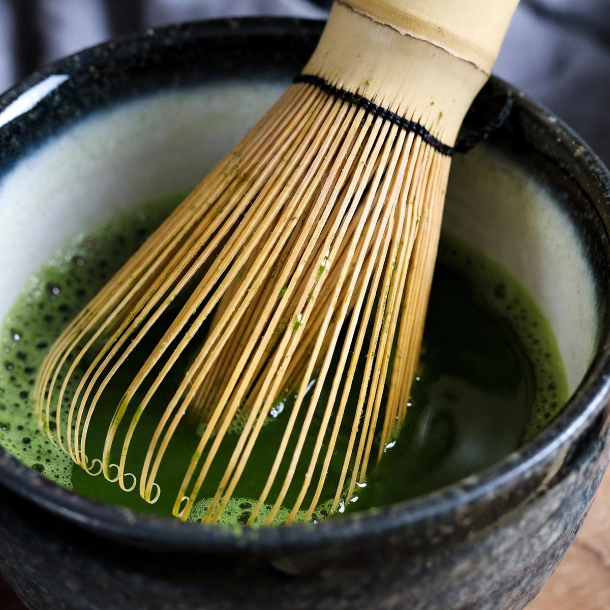Gros plan des brins fins et courbés du chasen Bambumie dans un bol de matcha