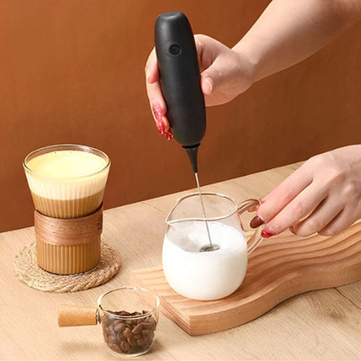 Mousseur électrique Mousso noir fouettant du lait dans un pichet en verre, café au lait à côté