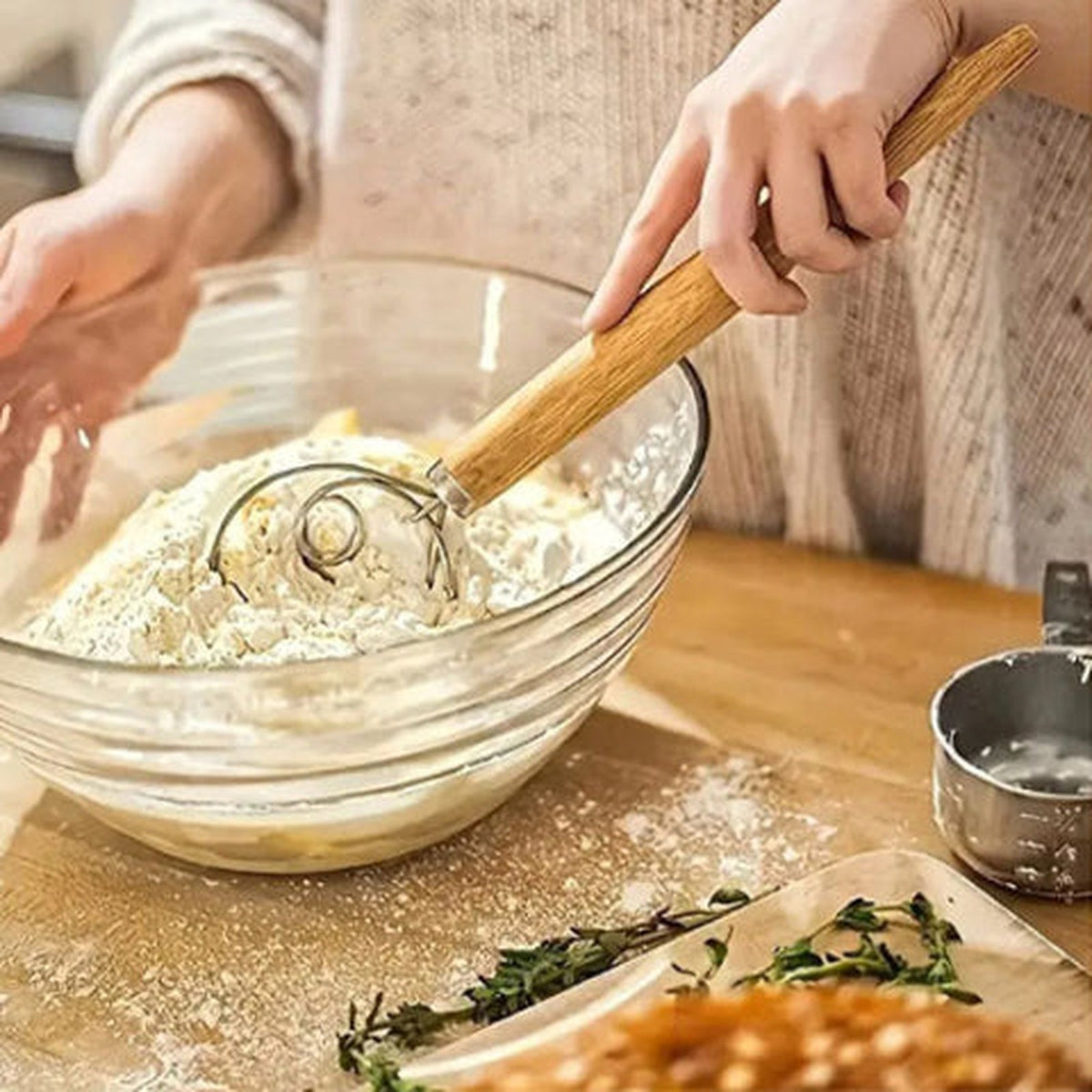 Mains travaillant une pâte à la farine au fouet danois dans un grand saladier en verre