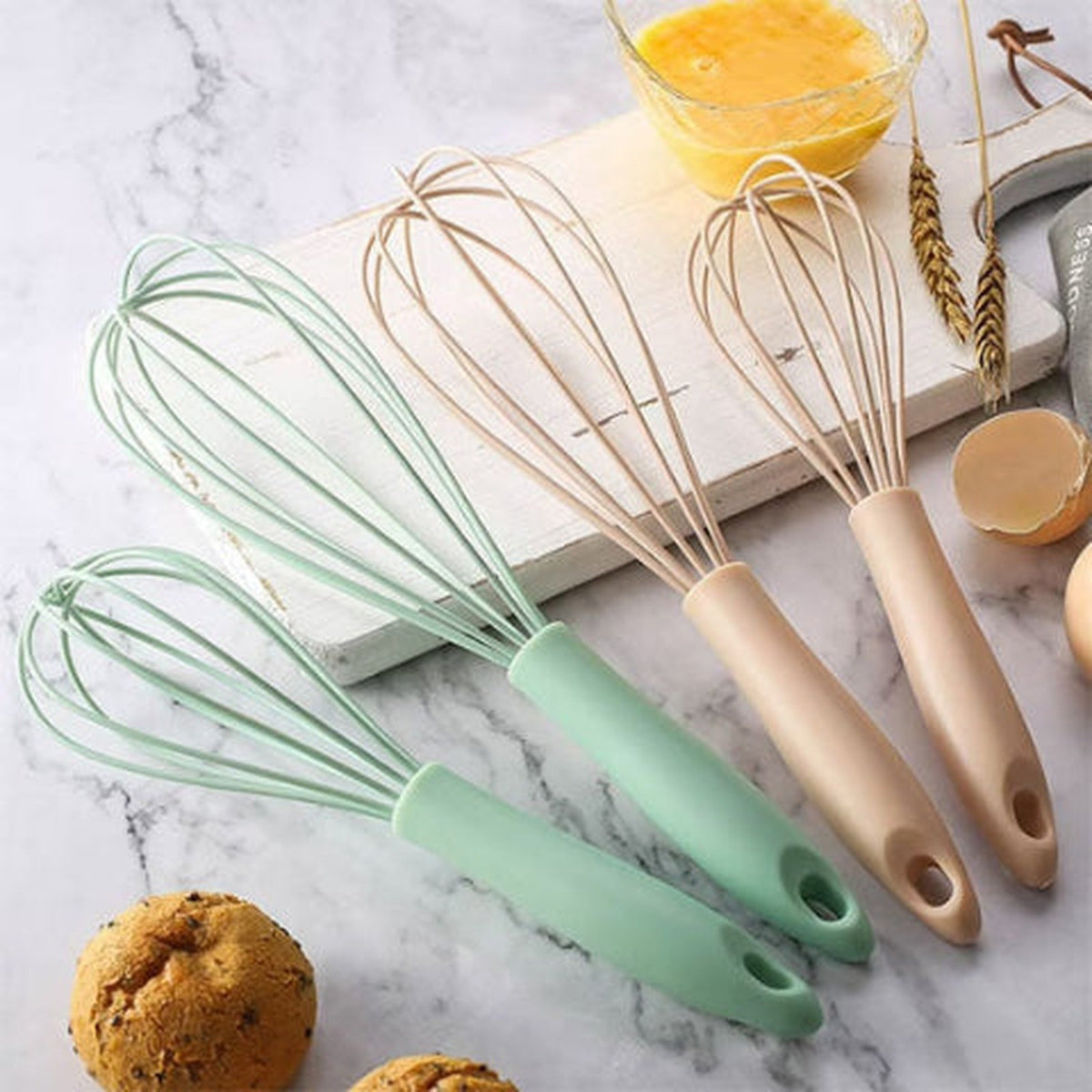 Fouets FlexiPro en silicone vert d'eau et rose posés côte à côte sur un marbre clair