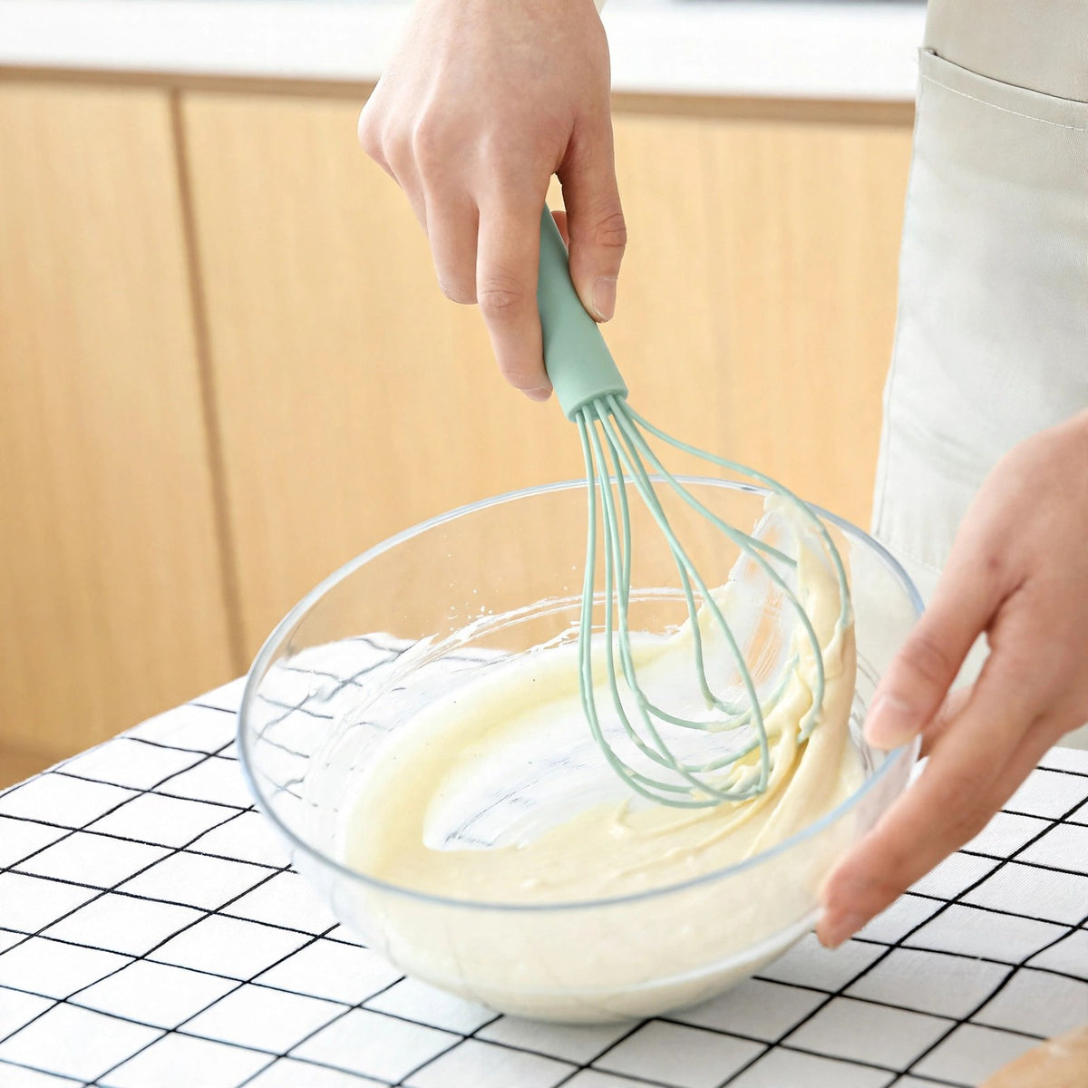 Fouet FlexiPro vert d'eau raclant une pâte à gâteau contre la paroi d'un bol en verre, fils flexibles