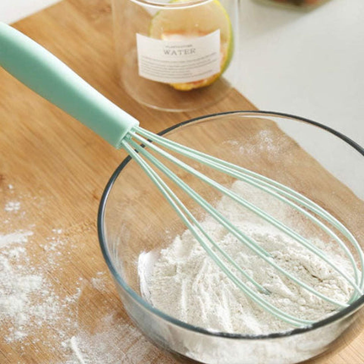 Fouet FlexiPro vert à plat dans un bol en verre de farine, fils souples gainés de silicone