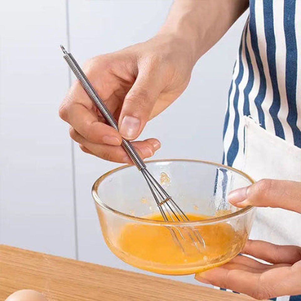 Fouet Fusion en inox battant un œuf dans un petit bol en verre tenu à la main