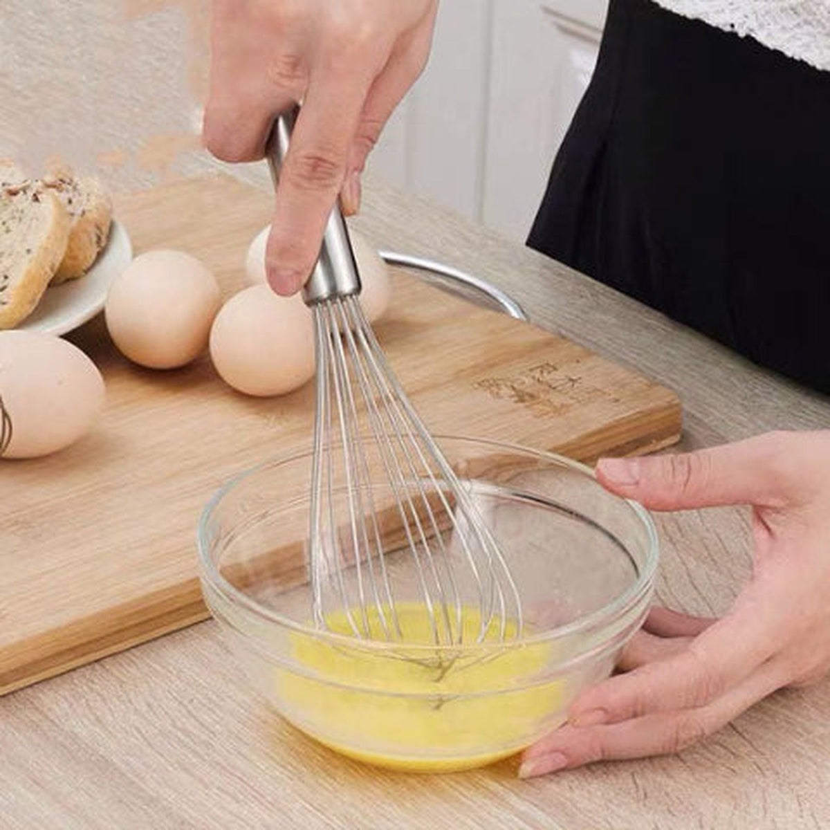 Fouet InoxStar en inox battant des œufs dans un bol en verre sur une planche en bois