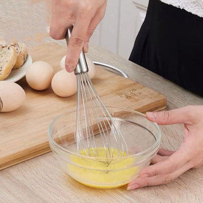 Fouet InoxStar en inox battant des œufs dans un bol en verre sur une planche en bois