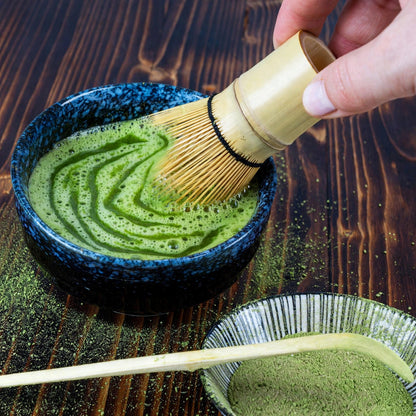 Chasen en bambou fouettant un matcha en zigzag dans un bol bleu nuit, mousse fine en surface