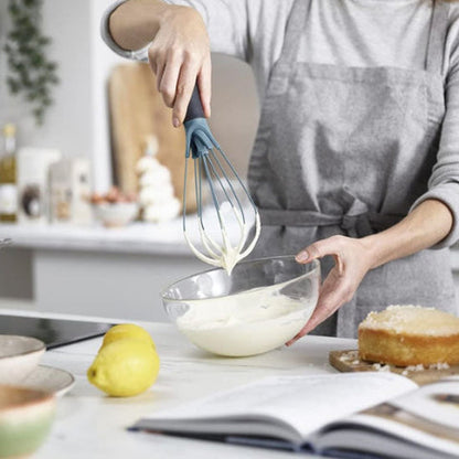 Fouet plat Aromova soulevant une crème dans un bol en verre, cuisine lumineuse et tablier gris