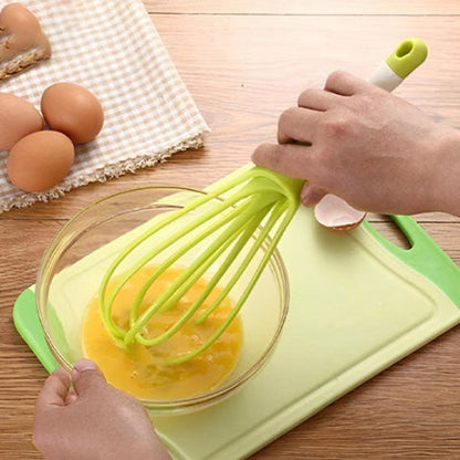 Fouet plat Aromova vert battant des œufs dans un bol en verre sur une planche de cuisine