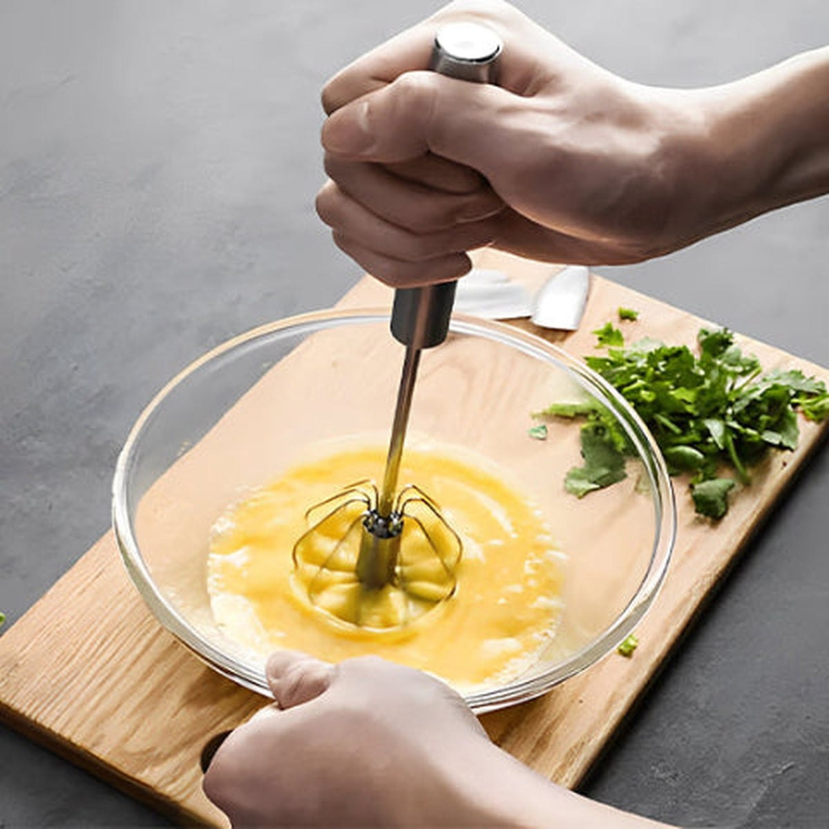 Fouet PushMix en inox en pleine pression dans un bol d'œufs battus, main sur le manche pompe