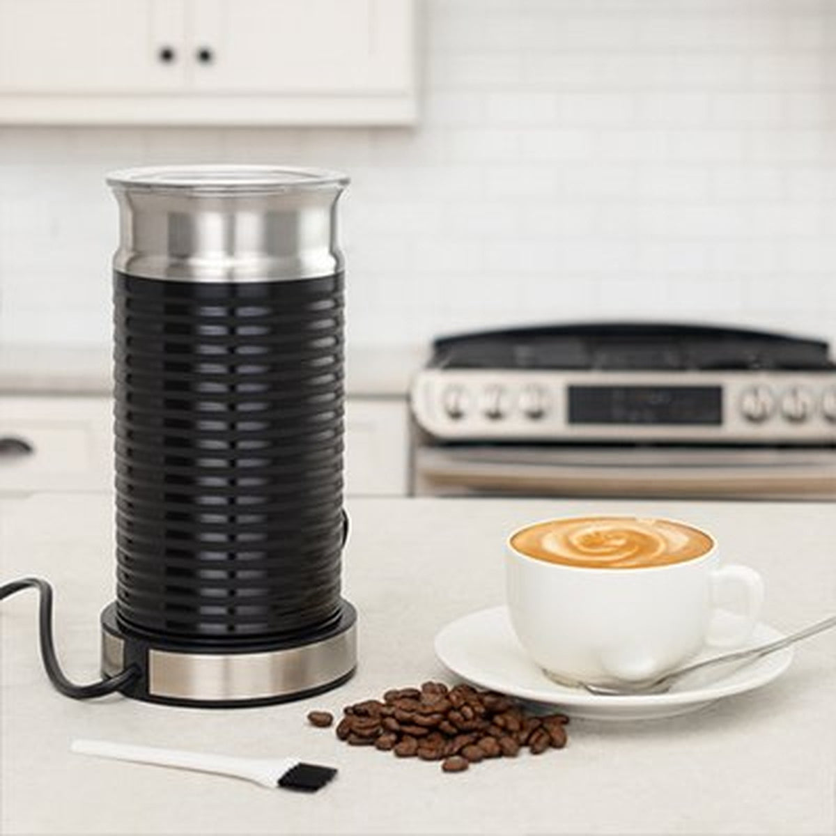 Mousseur à lait électrique noir sur un plan de travail, cappuccino et grains de café à côté