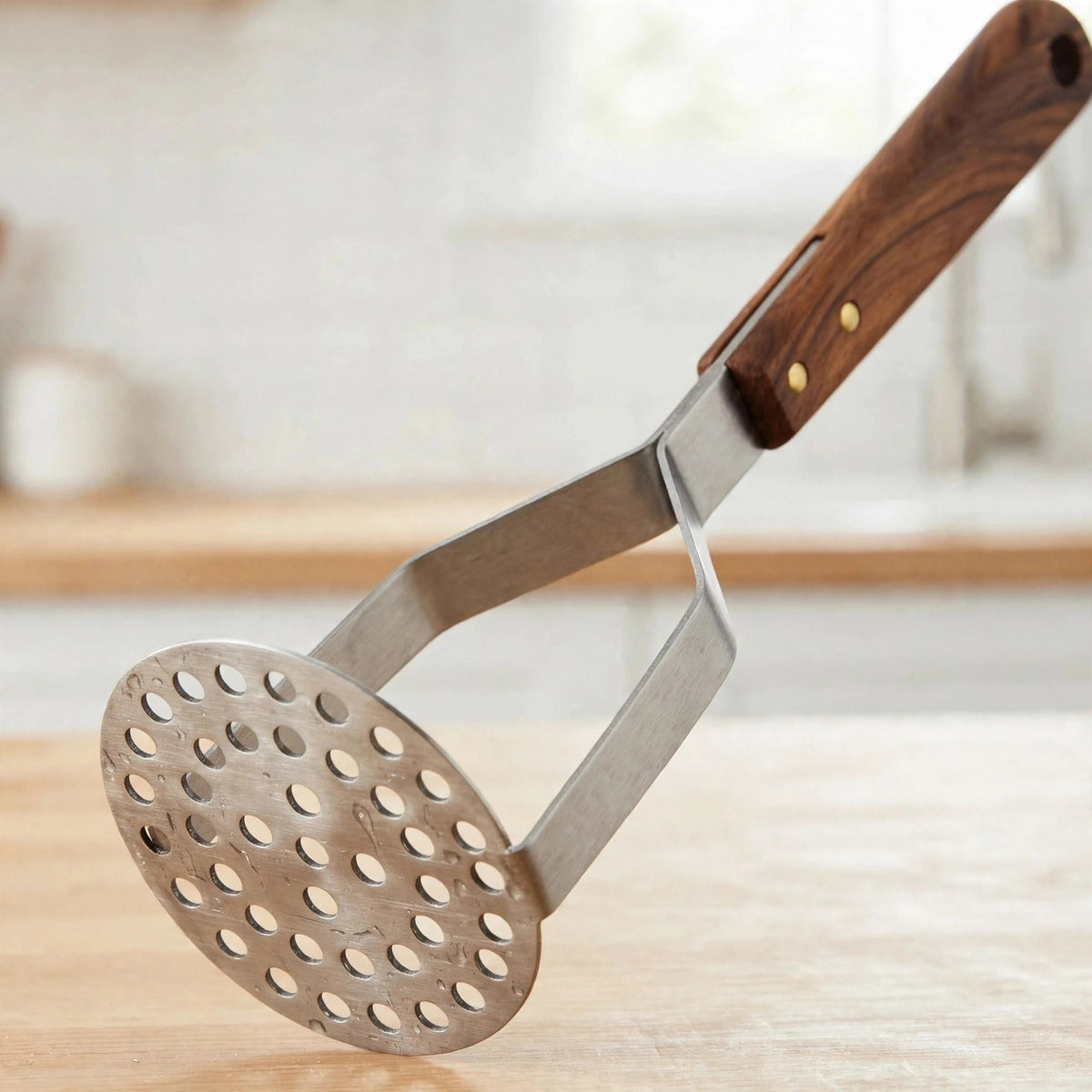 Détail de la plaque ronde perforée en inox et de la jonction manche en bois à rivets du presse-purée
